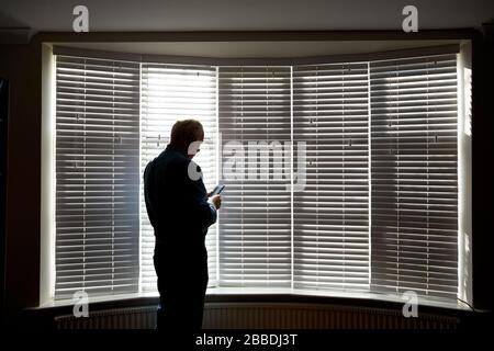 Foto eines Mannes in Schilouette vor einem großen Fenster während der Isolation von UK Covid 19. Stockfoto