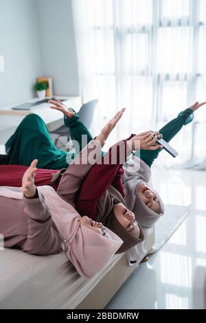 Drei verschleierte Frauen legten sich auf und die Hände hoben sich auf das Bett, während sie zusammen mit dem Kamerasmartphone eine selfie nahmen Stockfoto