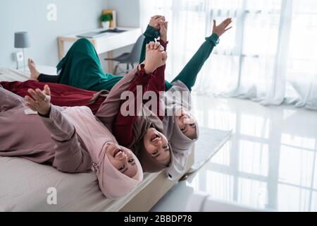 Drei verschleierte Frauen legten sich auf und die Hände hoben sich auf das Bett, während sie zu Hause Spaß hatten Stockfoto