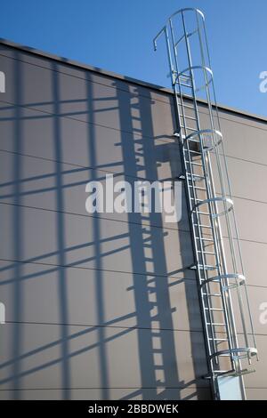 Flucht- oder Rettungsleiter in einem modernen Industriegebäude mit Schatten an der Wand Stockfoto