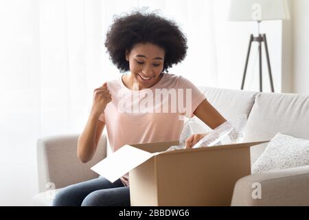 Die afroamerikanische Frau öffnet eine Schachtel und freut sich Stockfoto