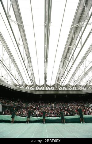 Groundstaff Race, um die Abdeckungen auf dem Mittelplatz zu platzieren, während Regen das Spiel während des Spiels zwischen der polnischen Agnieszka Radwanska und der französischen Frau de Johansson während des vierten Tages der Wimbledon Meisterschaften im All England Lawn Tennis and Croquet Club, Wimbledon, unterbricht. Stockfoto