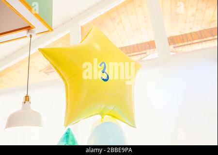 Großer Ballonstern aus gelber Folie mit der Nummer drei im Raum. Stockfoto