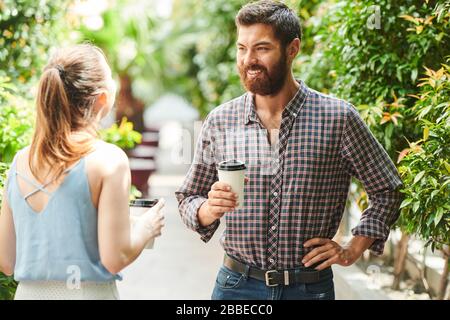 Selbstbewusster lächelnder bärtiger Mann im Plaid Shirt, der Tasse Kaffee wegnimmt und mit einer Freundin spricht Stockfoto