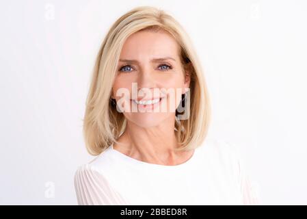Nahaufnahme des Porträts der schönen älteren Frau, die die Kamera betrachtet und lächelt, während sie auf einem isolierten weißen Hinterteil steht. Stockfoto