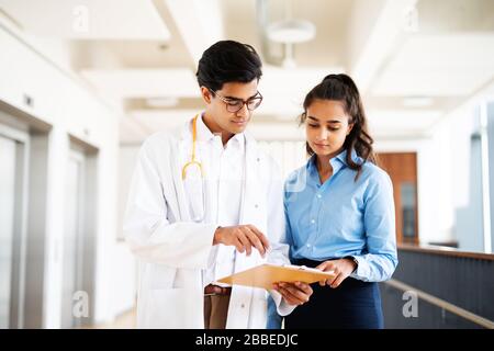 Zwei junge Ärzte diskutieren im Flur in einem Krankenhaus über etwas Stockfoto