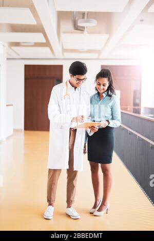 Zwei junge Ärzte diskutieren im Flur in einem Krankenhaus über etwas Stockfoto