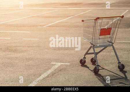 Leerer Einkaufswagen auf einem leeren Parkplatz in der Nähe eines Supermarktes, ohne Menschen bei Sonnenuntergang. Stockfoto