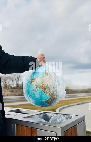 Mann wirft einen Globus, der in Plastiktüten verpackt ist, in den Müll. Konzept der Kunststoffverschmutzung und des Recycling von Kunststoffabfällen. Umweltproblem. Umweltstaudamm Stockfoto