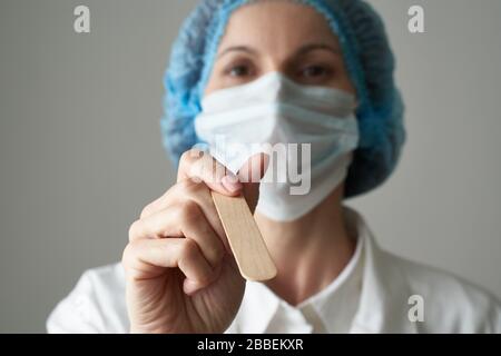 Weibliche Ärztin in medizinischer Maske und Uniform prüfen den Zustand der Kehle. Krankheit und Bündnisschutz, medizinische Sicherheit. Nahaufnahme Stockfoto