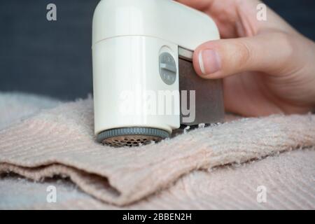 Pullover mit Pillerfüllung. Frau Hand mit dem tragbaren Rasierer Fuzz-Remover-Gerät für elektrische Gewebe, um Fuzz, Flusen und Pillen (Pilling) auf der Kleidung zu entfernen Stockfoto