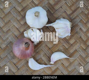 Eine rote, mittelgroße frische Zwiebel und etwas weißer Knoblauch neben einigen verstreuten Knoblauchsaaten auf Holzhintergrund Stockfoto