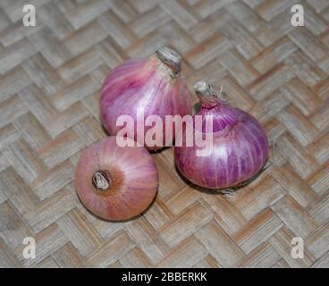 Draufsicht von drei mittelgroßen, rot gefärbten frischen Zwiebeln, die sich auf einem Holzteppichhintergrund versammelt haben Stockfoto