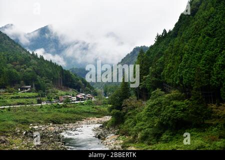 Üppige grüne Landschaft entlang der Takayama-Linie und des Flusses Hida auf dem Weg nach Takayama mit tief hängenden Wolken, die über die Bergketten drapiert sind Stockfoto