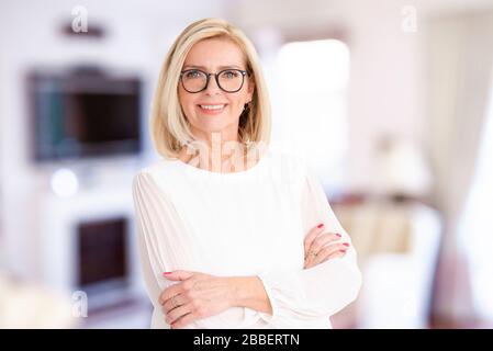 Portraitaufnahme einer schönen Dame, die mit den Armen in der Halle steht, während sie die Kamera betrachtet und lächelt. Stockfoto