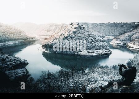 Fotograf fotografiert in einer verschneiten Landschaft eines Flussmäanders Stockfoto