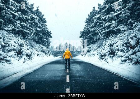 Person mit gelbem Mantel inmitten einer Straße inmitten eines Schneesturms in einer Winterlandschaft Stockfoto