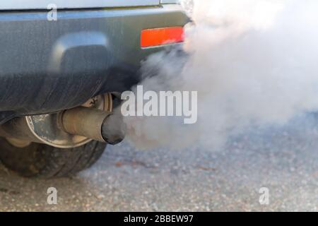 Starker Rauch raucht auf einem Auto vom Abgashaufen. Geringe Schärfentiefe, Fokus auf das Ende des Leitrohrs. Nahansicht. Stockfoto