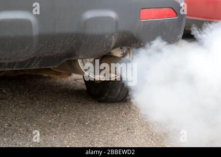 Starker Rauch raucht auf einem Auto vom Abgashaufen. Geringe Schärfentiefe, Fokus auf das Ende des Leitrohrs. Nahansicht. Stockfoto