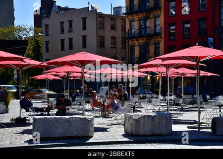 New York, USA: Blick auf den Platz mit roten Sonnenschirmen an der Kreuzung von 9th Av und 14th Street; Menschen in der Sonne entspannen Stockfoto