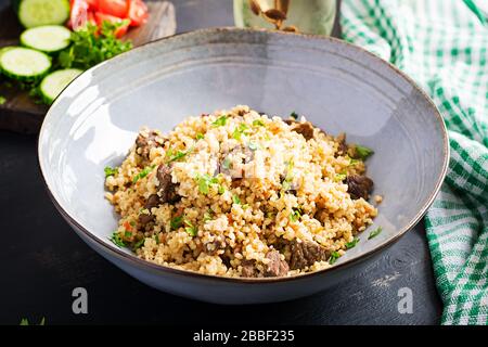 Bulgur Pilaf mit Fleisch und Gemüse. Köstliches warmes Mittagessen auf schwarzem Hintergrund. Östliche Küche. Stockfoto