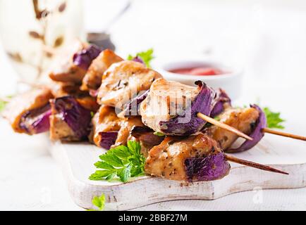 Gegrilltes Hühnerkebab mit roten Zwiebeln auf einem hellen Tisch. Gegrillte Fleischspieße, schischiger Kebab auf hellem Hintergrund. Stockfoto
