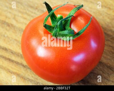 Eine einzelne reife rote Tomate mit Stielchen auf einem Holzhackbrett Stockfoto