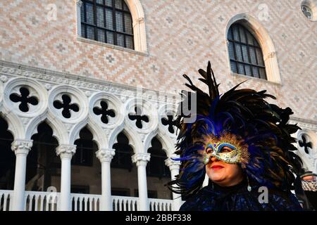 Venedig, Italy-Februar 2020; niedriger Blickwinkel auf eine Frau mit Maske für den traditionellen Maskenball für den Karneval gegen die Fassade des Dogenpalastes Stockfoto