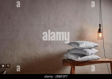 Leerer Naturputz unregelmäßige unebene Wand hängende Glühbirne Kissen Hocker Stockfoto