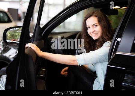 Fröhlich lachende junge Frau sitzt in einem neuen Auto in einem Autohaus Stockfoto