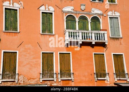 Nahaufnahme eines Abschnitts eines historischen Gebäudes in Venedig mit einer großen Anzahl verwitterter Blenden gegen eine Wand mit etwas verblichener Kogel Stockfoto