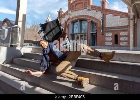 Behinderter Latino-junger Mann im Rollstuhl fällt eine Treppe hinunter, die er nicht mit dem Stuhl auf der Straße hinuntergehen kann Stockfoto