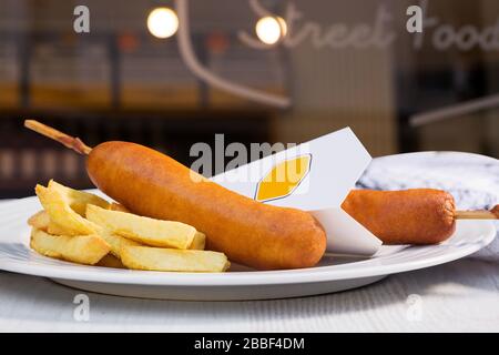 Traditionelle amerikanische Straßennahrung Maishunde mit pommes frites auf weißem Teller. Essen auf der Straße mitnehmen. Stockfoto