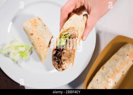 Burrito wickelt sich mit gezogenem Schweinefleisch, Bohnen, Reis und Gemüse auf weißem Teller. Mexikanische Küche. Stockfoto