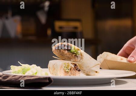 Burrito wickelt sich mit gezogenem Schweinefleisch, Bohnen, Reis und Gemüse auf weißem Teller. Mexikanische Küche. Stockfoto