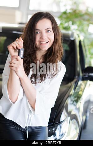 Attraktive junge Frau lacht glücklich in einem Auto in einem Autohaus und hält den Autoschlüssel Stockfoto