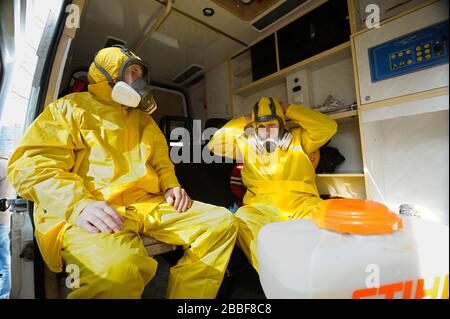 Sanitäter sitzen im Rettungswagen und tragen gelbe Schutzkleidung und Masken zur Desinfektion von Coronavirus auf. Februar 2020. Kiew, U Stockfoto