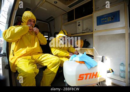 Sanitäter sitzen im Rettungswagen und tragen gelbe Schutzkleidung und Masken zur Desinfektion von Coronavirus auf. Februar 2020. Kiew, U Stockfoto