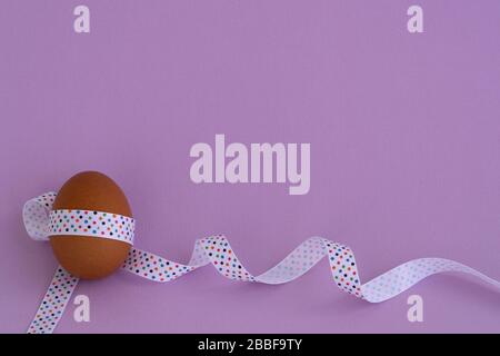 Ei steht auf Becher, auf weichem violettem Hintergrund. Osterei mit festlichem Band gefesselt Stockfoto