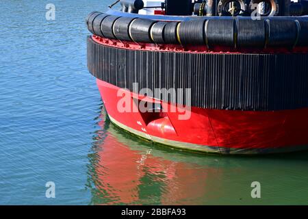 Close up view of a section of the bow of a large red tug boat in Rotterdam Europoort. Showing large rubber tug boat fenders for protection Stockfoto