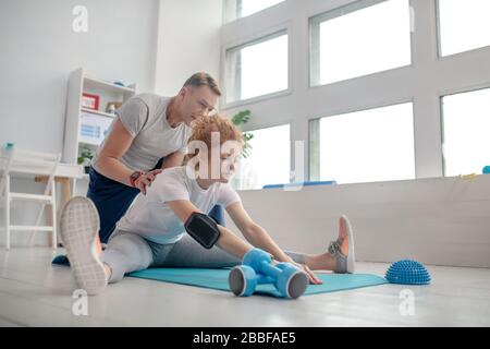 Weibliche Patientin spaltet auf Matte, männliche Physiotherapeutin hilft ihr Stockfoto