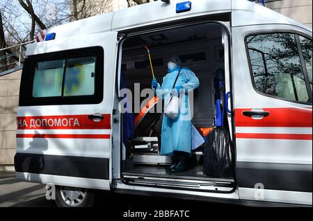 Sanitäter in Schutzmaske und Kostüm desinfizieren den Rettungswagen mit der Spritze Stockfoto