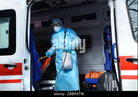 Sanitäter in Schutzmaske und Kostüm desinfizieren den Rettungswagen mit der Spritze Stockfoto