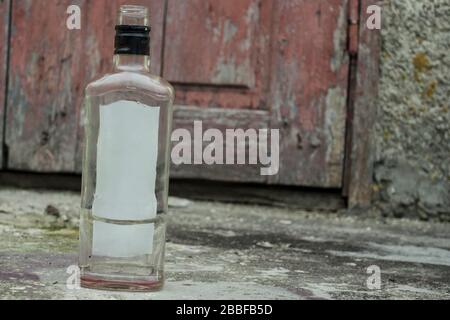 Leere Glasflasche auf dem Hintergrund braun gerissener Türen, Entlöschung, Alkoholismus, ein wenig verschwommener Hintergrund Stockfoto