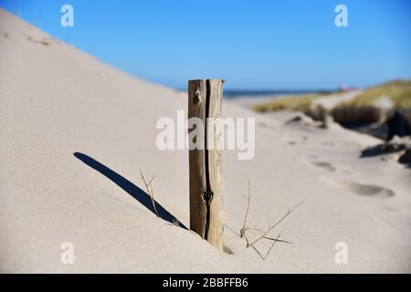 Nahaufnahme des Holzpfahls in einem sandigen Maavlakte-Strand an einem sonnigen Tag mit langem Schatten im Sand und unscharfem blauem Hintergrund Stockfoto