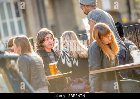 Die Sonne schillert auf einem Kellner, der Brille auf der Terrasse einer kühlen und geschäftigen East London Bar in Hackney Wick sammelt. Stockfoto