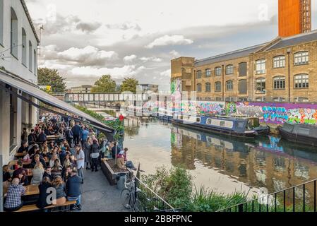 Gruppen junger Flusspferde unterhalten sich an einer Bar am Flussufer und einer Restaurantterrasse am Ufer des Flusses lea in Hackney Wick, East London, Großbritannien Stockfoto