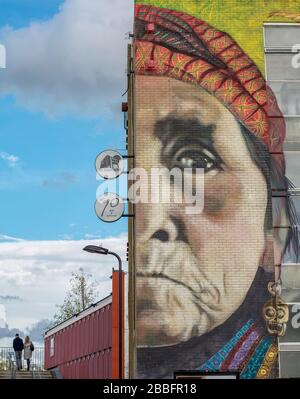 Ein Paar, das auf einer Brücke über den Fluss Lea in Hackney Wick im Osten Londons spazieren geht. Im Vordergrund steht ein Wandbild mit beauftragten Graffiti-Künstlern Stockfoto