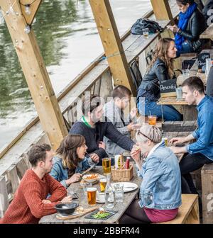 Gruppen junger Flusspferde unterhalten sich an einer Bar am Flussufer und einer Restaurantterrasse am Ufer des Flusses lea in Hackney Wick, East London, Großbritannien Stockfoto