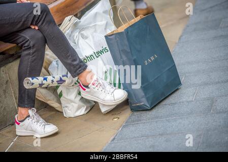 Ein Shopper nimmt Platz und ruht mit seinen Einkaufstaschen zu Füßen im Westfield Einkaufszentrum, Stratford East London Stockfoto